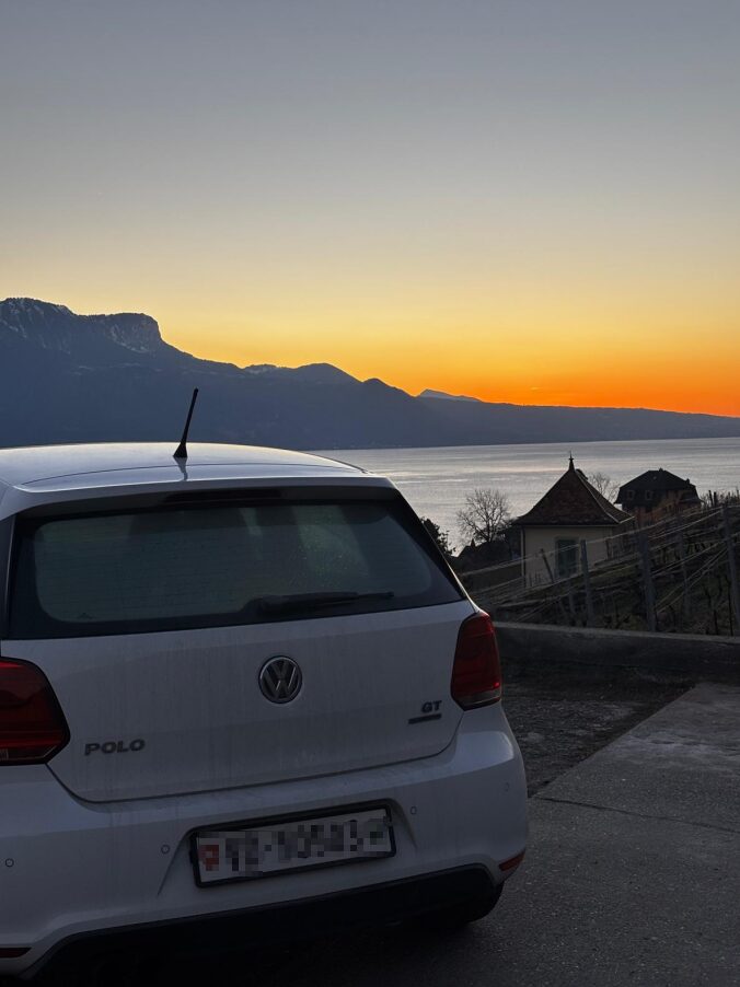 Volkswagen Polo GT blanche vue de l’arrière, devant un lac et des montagnes au coucher du soleil.